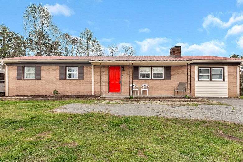 A charming brick ranch home presents a welcoming front porch, a bright red entry door, and a durable metal roof.