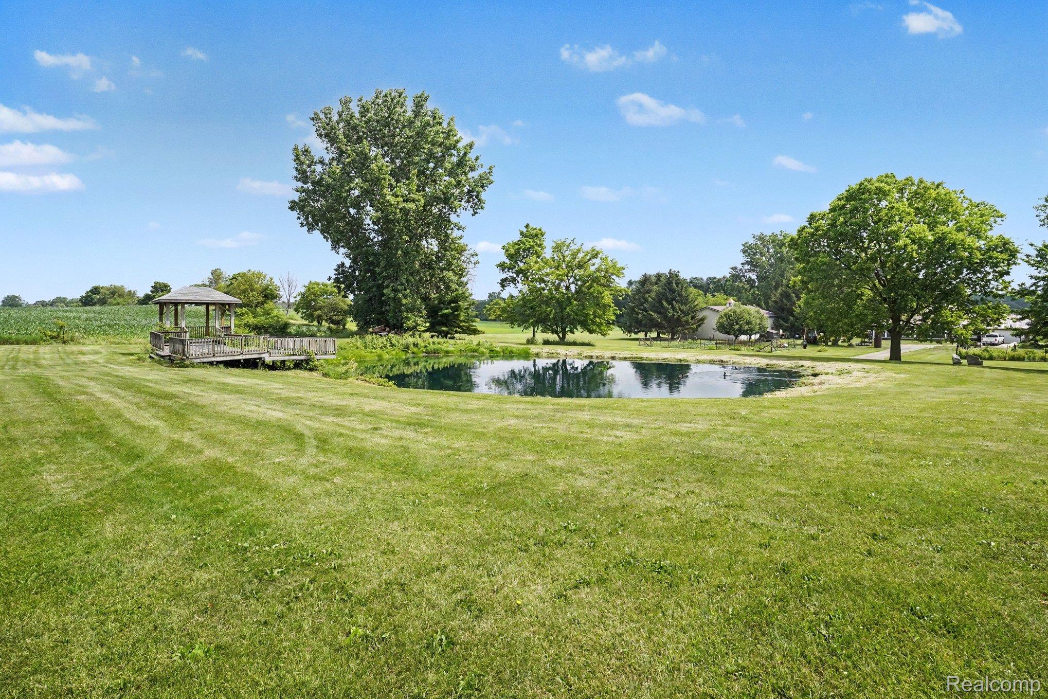 4848 Columbiaville Road Columbiaville, MI 48421 - Photo 26 of 35 Expansive grassy lawn featuring a private pond with a wooden gazebo and dock structure