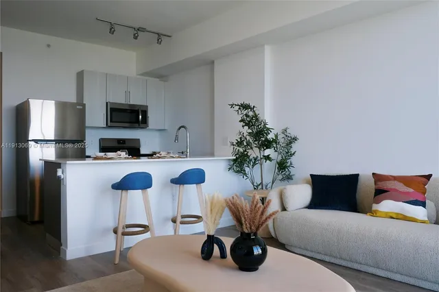 a living room with furniture a kitchen view and a refrigerator