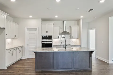 a large kitchen with stainless steel appliances granite countertop a stove a sink a refrigerator and white cabinets with wooden floor