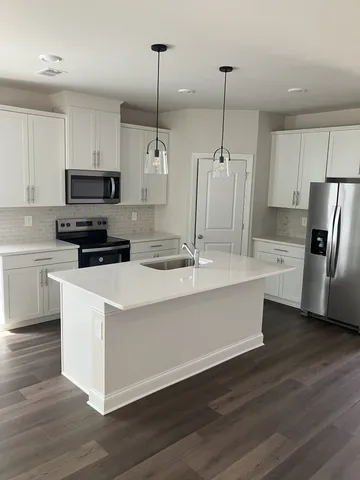 a kitchen with stainless steel appliances a stove a sink a refrigerator a center island and a wooden floor