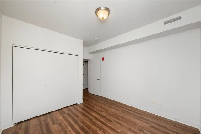a view of an empty room with wooden floor and fan