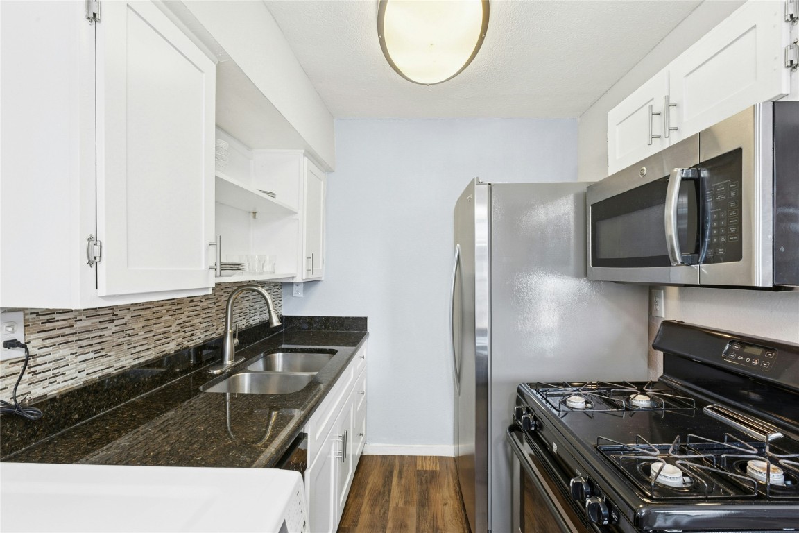 2401 Manor Road, Unit 214 Austin, TX 78722 - Photo 11 of 30 Kitchen with black gas range oven, white cabinets, dark stone counters, and stainless steel microwave