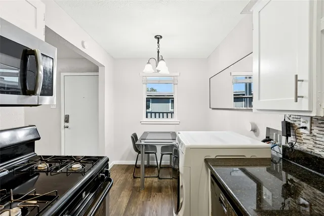 a kitchen with stainless steel appliances granite countertop a stove top oven a sink dishwasher and white cabinets with wooden floor