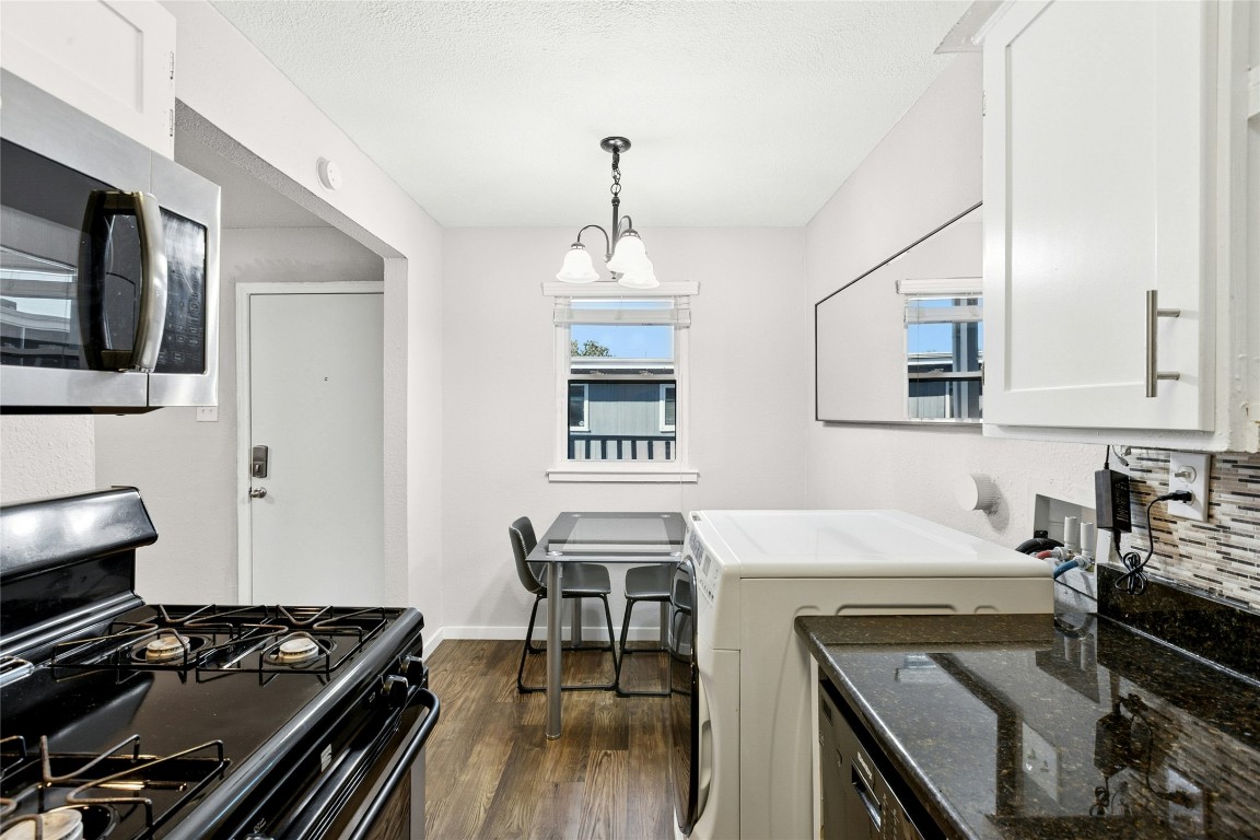 2401 Manor Road, Unit 214 Austin, TX 78722 - Photo 12 of 30 Kitchen featuring black range with gas cooktop, stainless steel microwave, dark wood-type flooring, decorative light fixtures, and washer / dryer