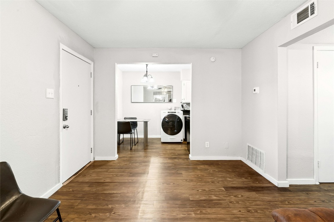 2401 Manor Road, Unit 214 Austin, TX 78722 - Photo 6 of 30 Laundry room featuring washer / dryer, dark wood finished floors, and a chandelier