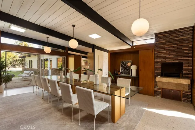 a dining room with wooden floor a chandelier fan a flat screen tv and a kitchen view