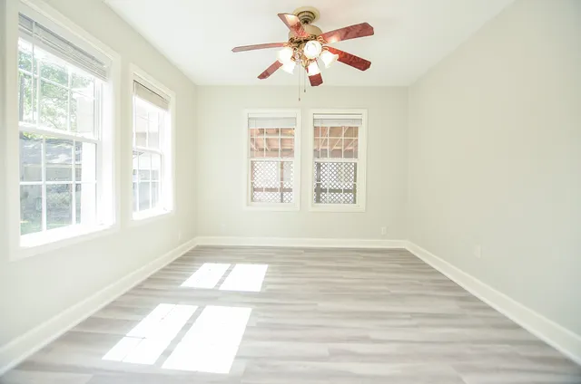 an empty room with wooden floor fan and windows