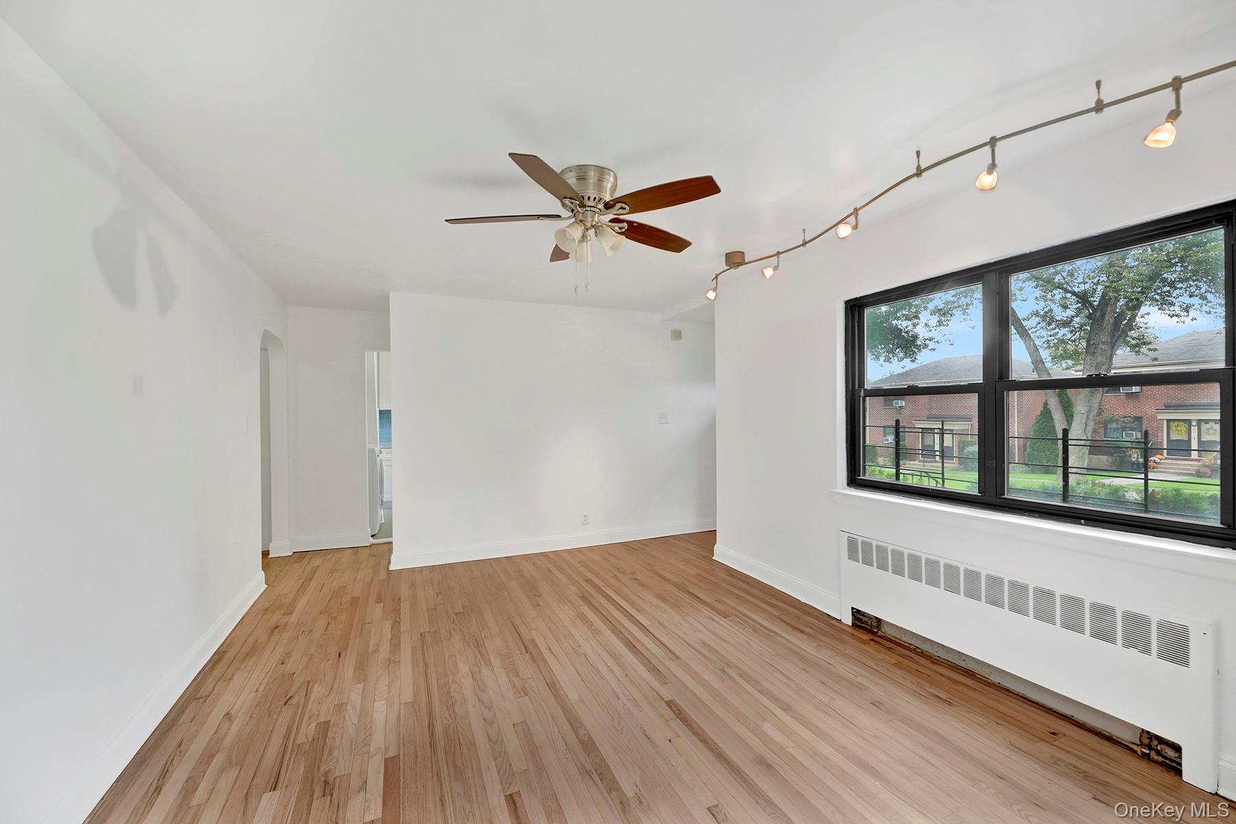 Unfurnished room featuring radiator heating unit, track lighting, light wood-style floors, and ceiling fan