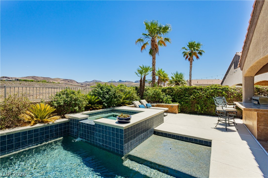 2256 Dogwood Ranch Avenue Henderson, NV 89052 - Photo 47 of 51 A desert oasis awaits with this sparkling pool, integrated spa, and an outdoor kitchen area set against a mountainous backdrop.