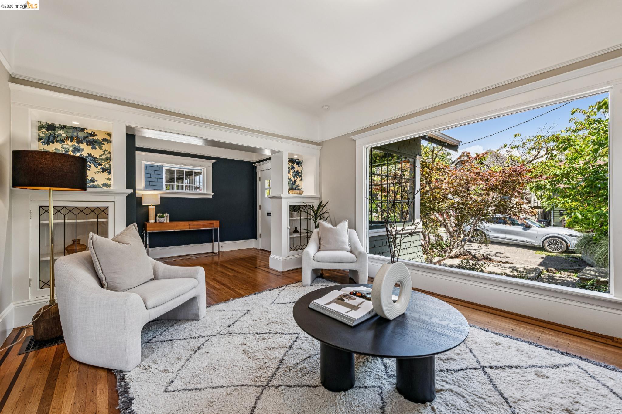 6521 Dover Street Berkeley, CA 94703 - Photo 12 of 80 Living area featuring wood-finish flooring, a large picture window, white trim detailing, and an arched entry to a secondary space