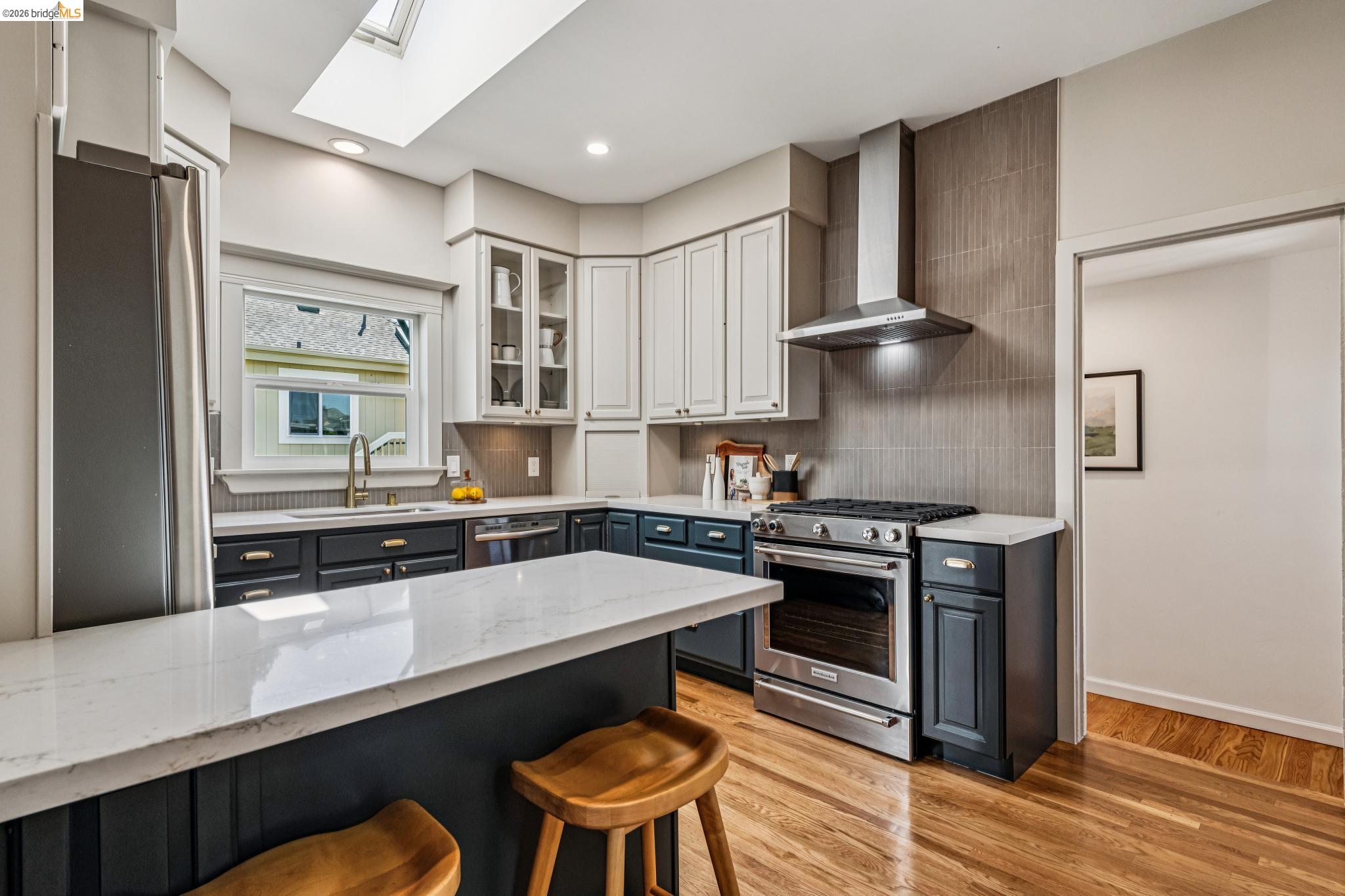 6521 Dover Street Berkeley, CA 94703 - Photo 20 of 80 Contemporary kitchen featuring a skylight, stainless steel appliances, two-tone cabinetry, quartz countertops, and wood-finish flooring