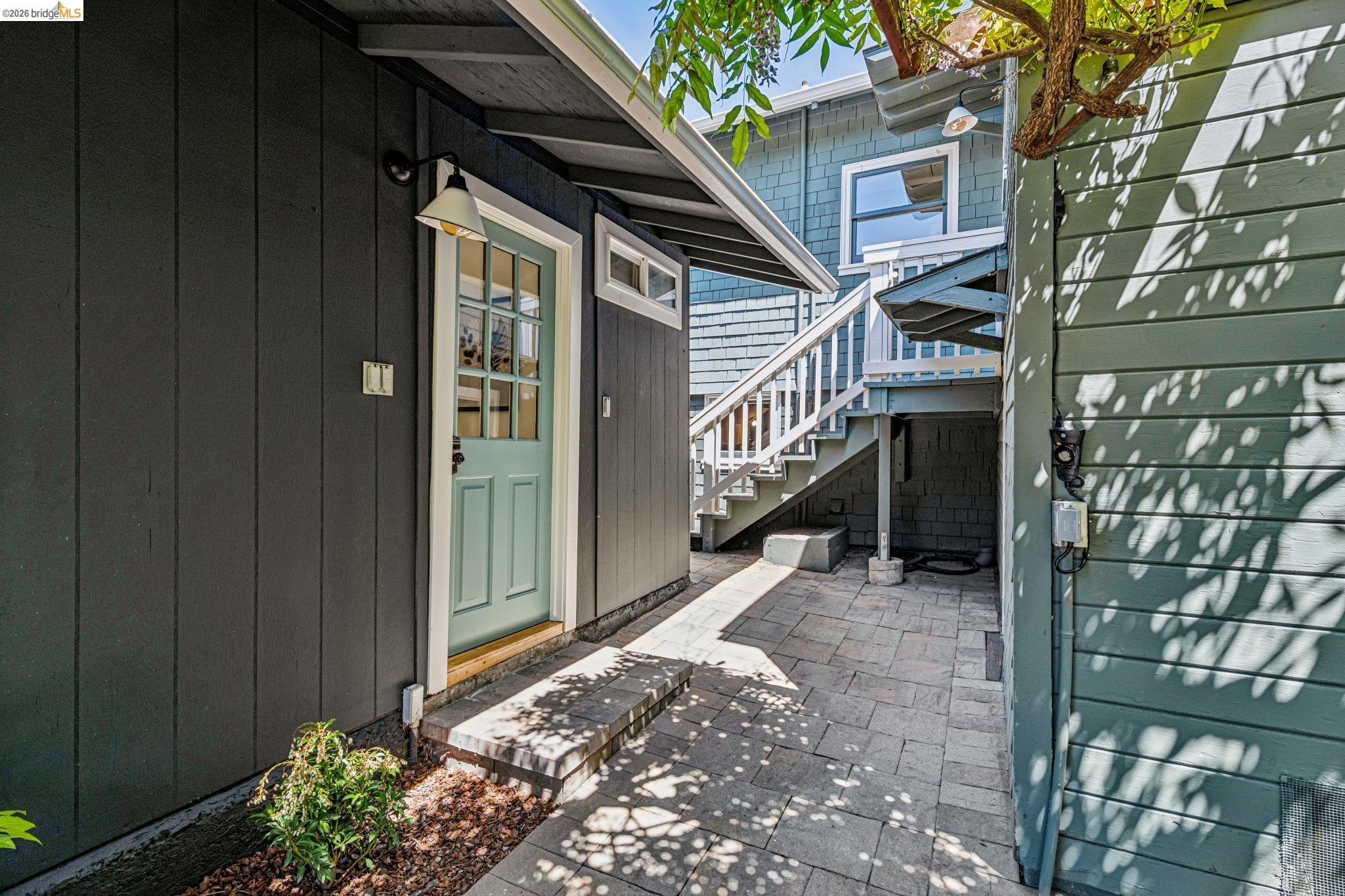 6521 Dover Street Berkeley, CA 94703 - Photo 35 of 80 Paved patio area featuring board and batten siding, a light green paneled door with windowpanes, and white-painted exterior stairs
