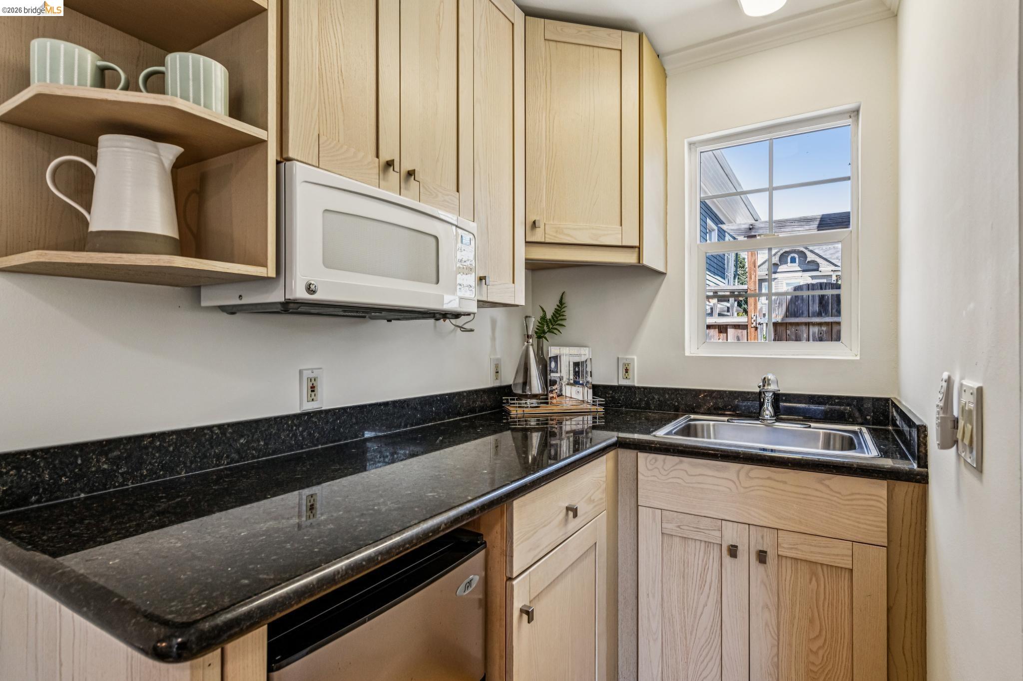 6521 Dover Street Berkeley, CA 94703 - Photo 44 of 80 Compact kitchen space featuring light wood-finish cabinetry, dark granite-style countertops, an undermount sink, and a built-in microwave