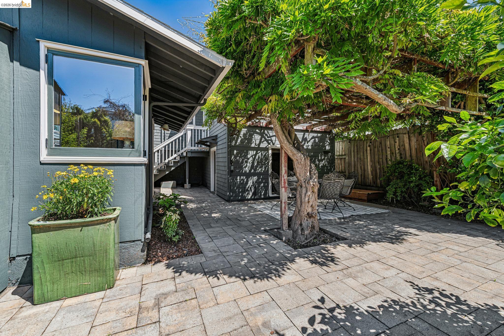 6521 Dover Street Berkeley, CA 94703 - Photo 45 of 80 Paver patio area featuring a mature tree providing natural shade, a building with dark siding, a wooden fence, and a white-trimmed window
