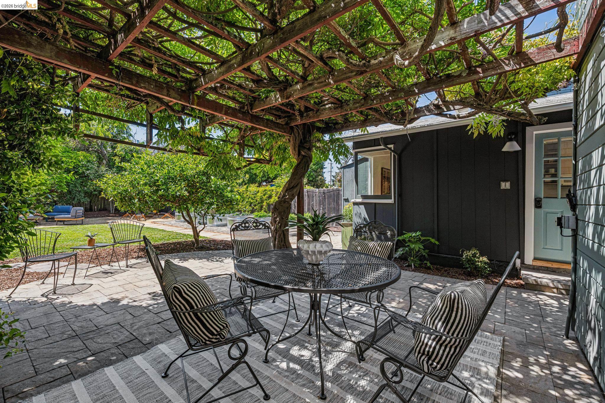 6521 Dover Street Berkeley, CA 94703 - Photo 48 of 80 Paved patio featuring a wood pergola with mature vines, a board and batten exterior, and a light blue entry door