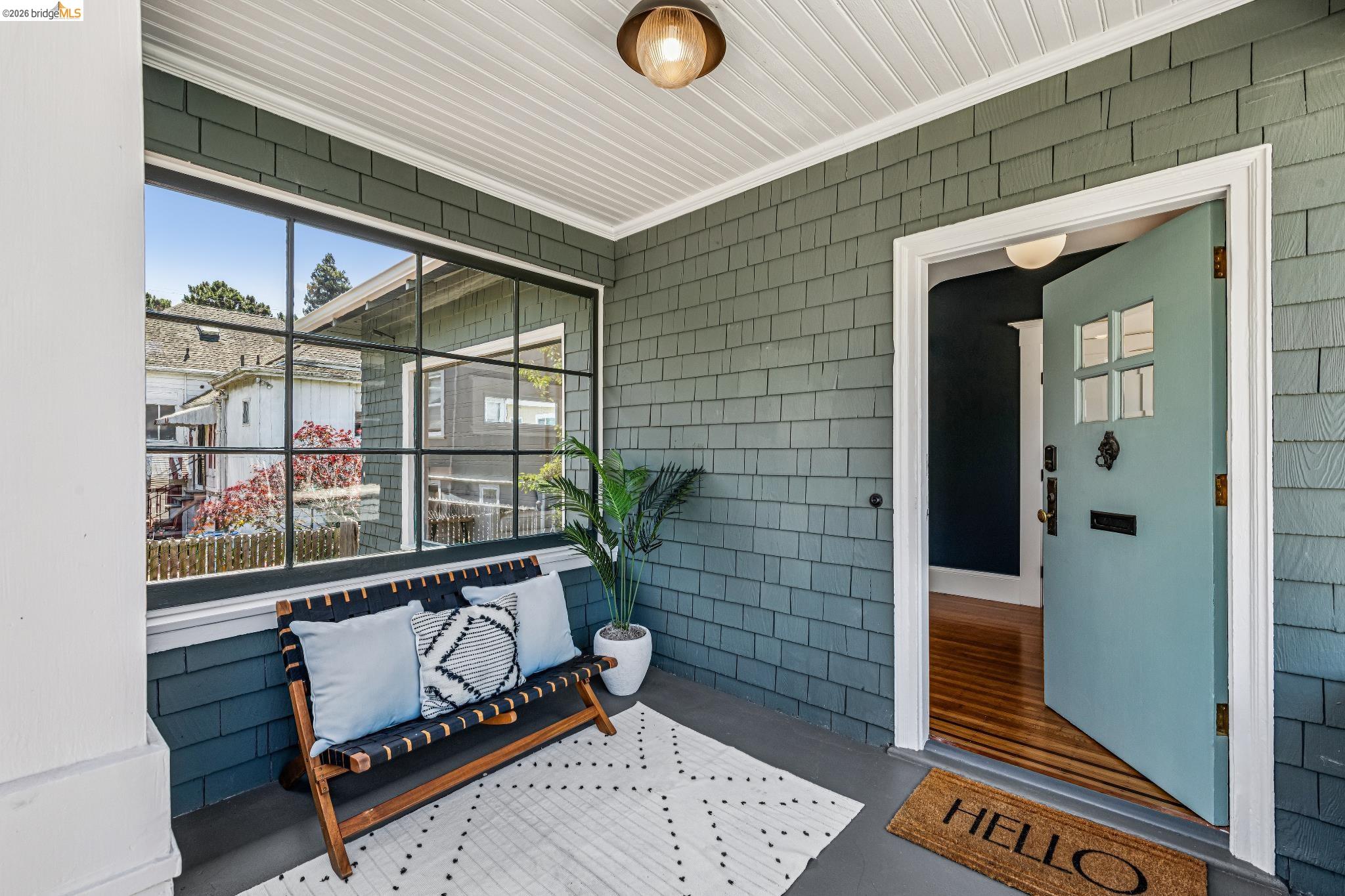 6521 Dover Street Berkeley, CA 94703 - Photo 5 of 80 Covered porch entry featuring a light blue paneled door with windowpanes, dark gray shingle siding, a large multi-pane window, and a beadboard ceiling with a flush-mount light fixture