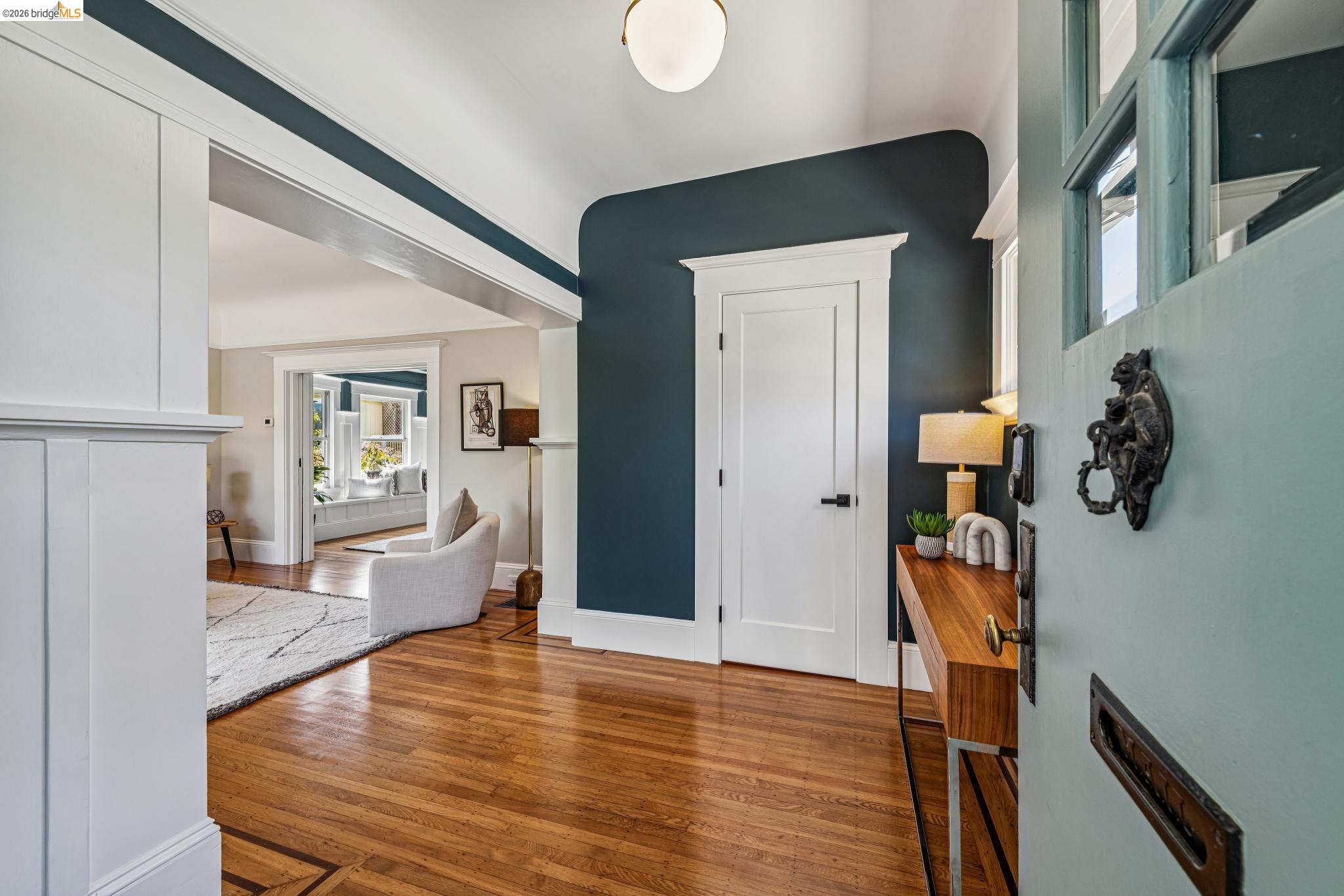 6521 Dover Street Berkeley, CA 94703 - Photo 9 of 80 Entryway featuring wood-finish flooring with inlay detail, a light blue paneled door with glass inserts, and a built-in wall panel with molding
