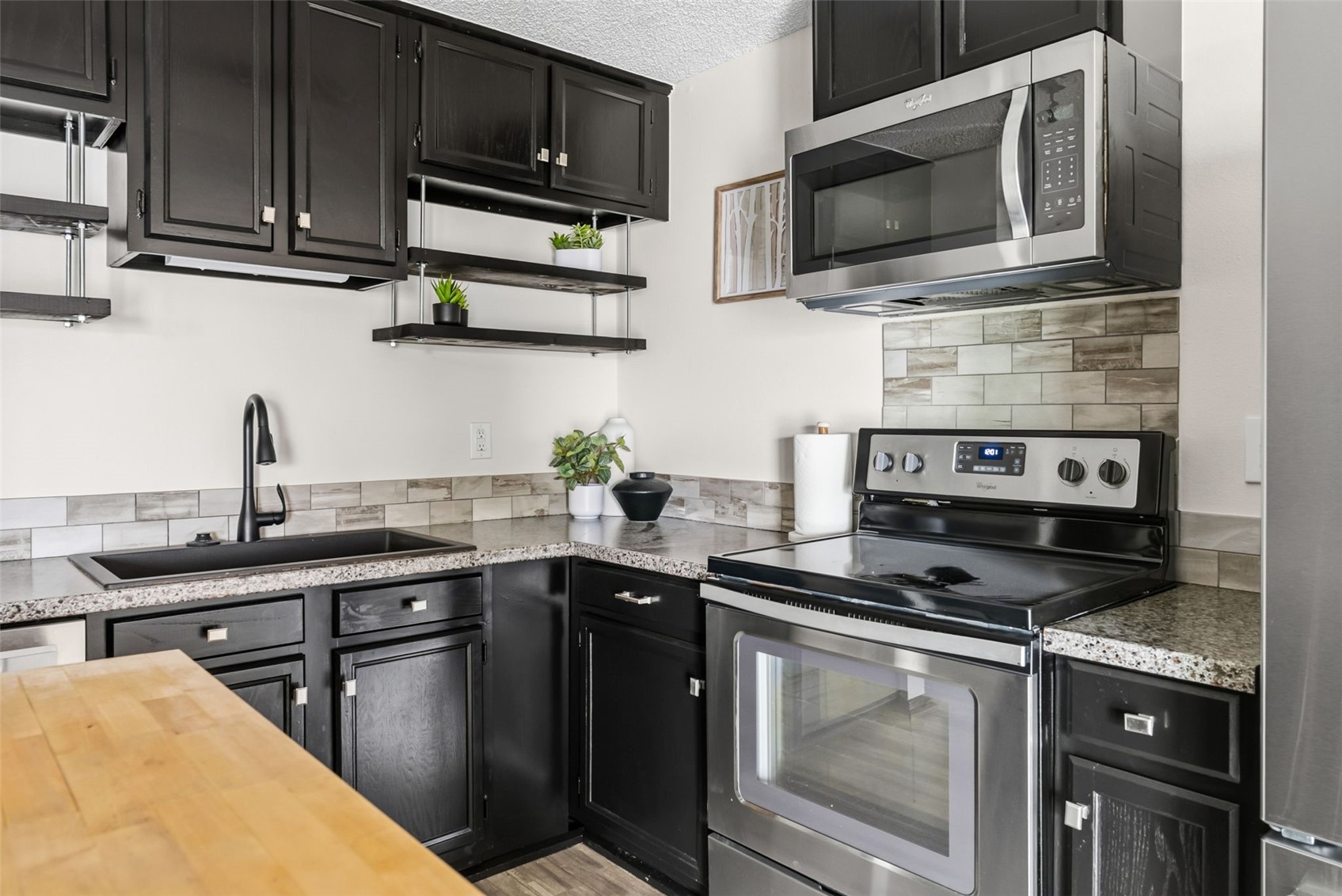 7124 Ryan Gulch Road, Unit 204 Wildernest, CO 80498 - Photo 19 of 36 Kitchen with dark cabinetry, stainless steel appliances, a textured ceiling, butcher block counters, and backsplash