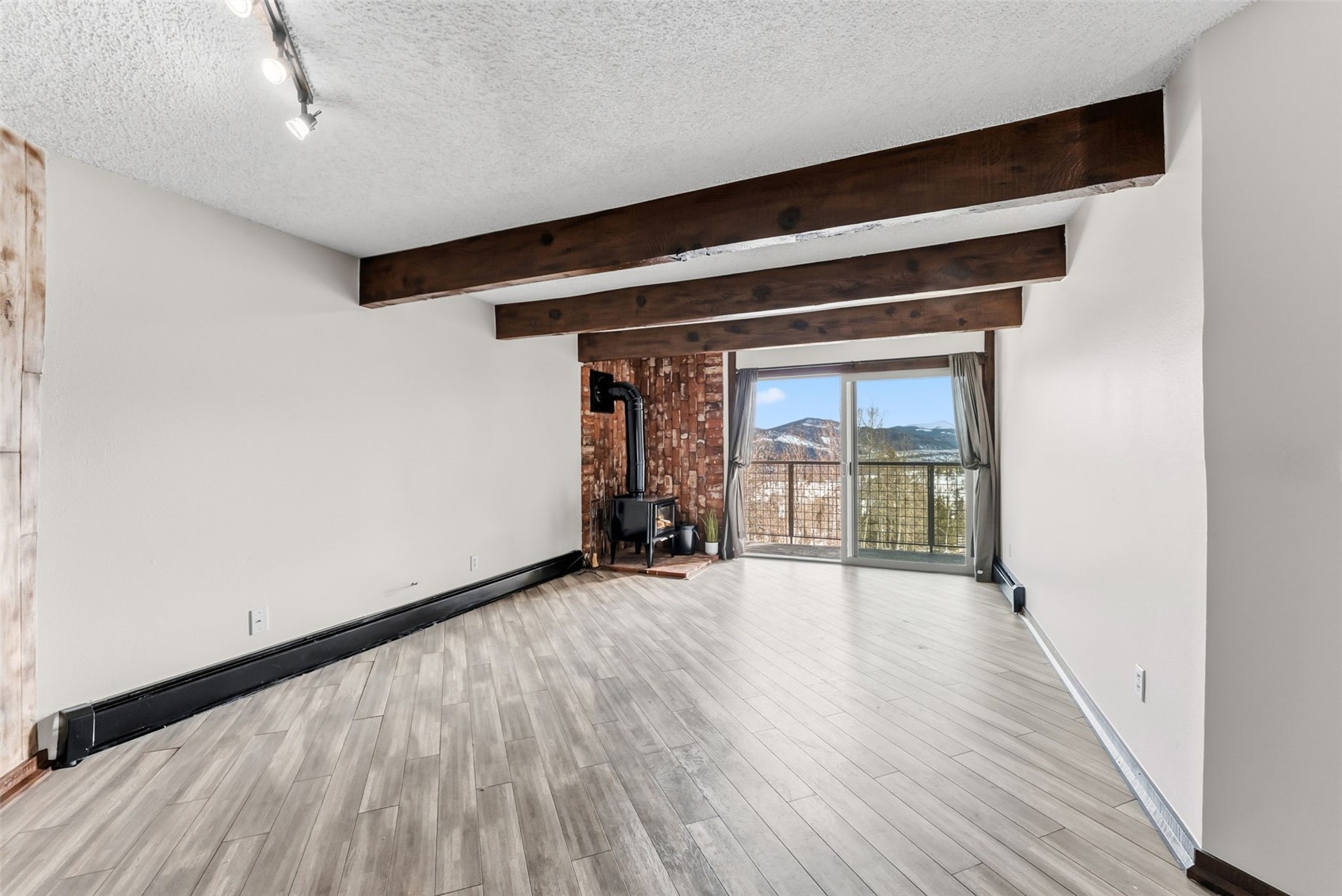 7124 Ryan Gulch Road, Unit 204 Wildernest, CO 80498 - Photo 6 of 36 Unfurnished living room with beam ceiling, a textured ceiling, a wood stove, wood finished floors, and a mountain view