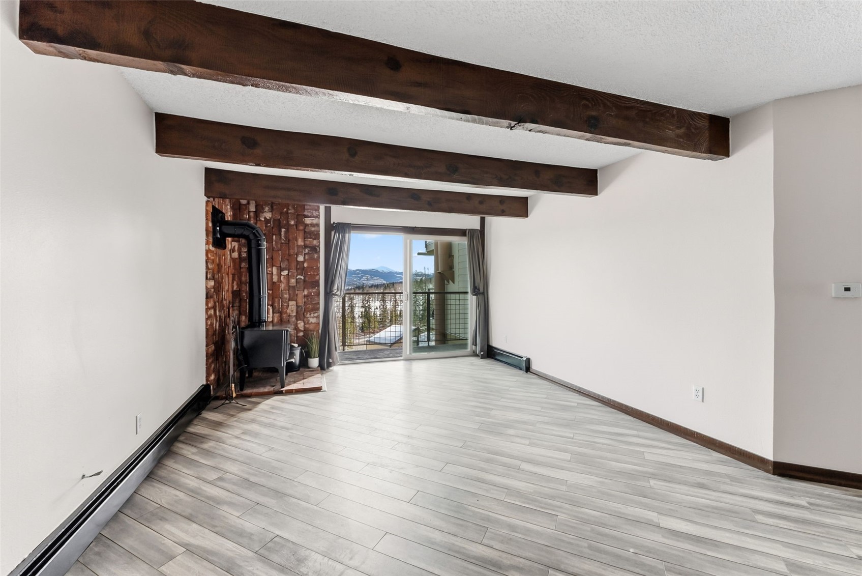 7124 Ryan Gulch Road, Unit 204 Wildernest, CO 80498 - Photo 7 of 36 Empty room featuring a baseboard radiator, a wood stove, light wood-style floors, a textured ceiling, and beamed ceiling