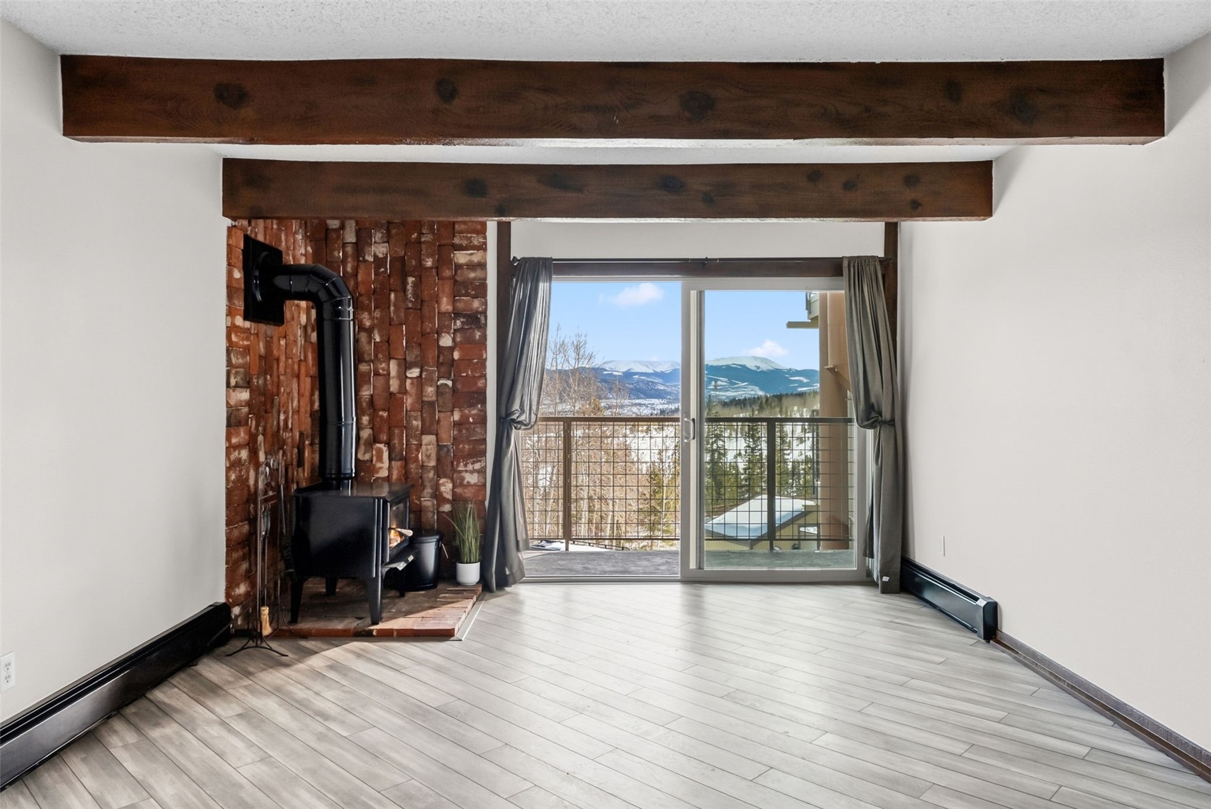 7124 Ryan Gulch Road, Unit 204 Wildernest, CO 80498 - Photo 8 of 36 Unfurnished living room featuring beamed ceiling, a wood stove, a mountain view, a textured ceiling, and baseboard heating