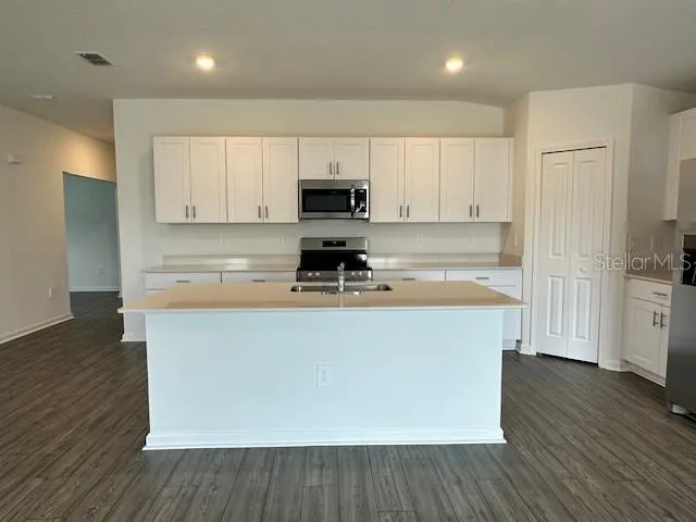 a kitchen with stainless steel appliances granite countertop a refrigerator a sink dishwasher a stove top oven a refrigerator with white cabinets and wooden floor