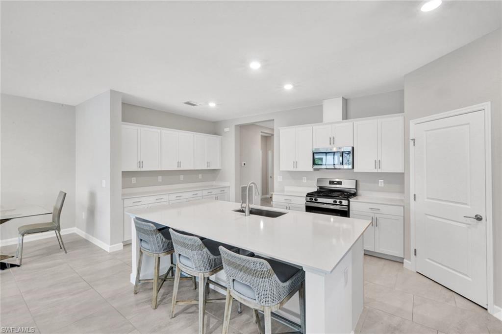 18298 Ridgeline Drive Estero, FL 33928 - Photo 14 of 49 Kitchen featuring stainless steel appliances, a kitchen breakfast bar, white cabinetry, an island with sink, and light stone countertops