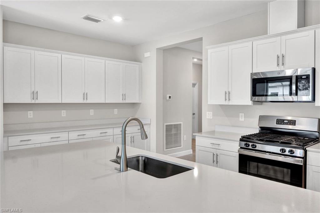 18298 Ridgeline Drive Estero, FL 33928 - Photo 15 of 49 Kitchen featuring stainless steel appliances, white cabinets, and light stone countertops