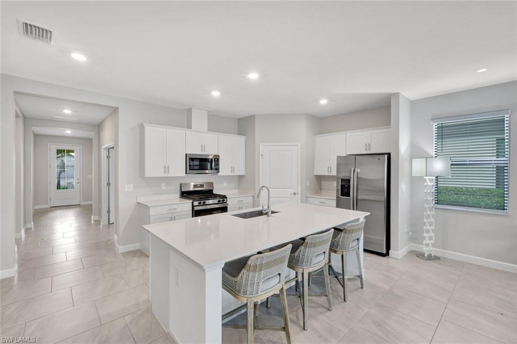 18298 Ridgeline Drive Estero, FL 33928 - Photo 16 of 49 Kitchen with white cabinets, stainless steel appliances, a breakfast bar area, a kitchen island with sink, and recessed lighting