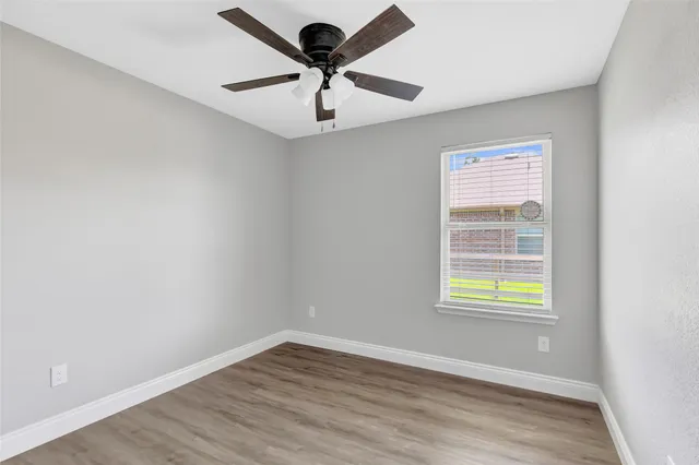 an empty room with wooden floor ceiling fan and windows