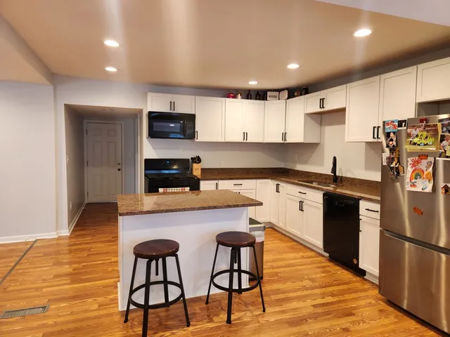 a kitchen with stainless steel appliances granite countertop a stove a sink a microwave a refrigerator and white cabinets with wooden floor