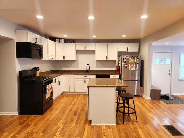 a kitchen with stainless steel appliances kitchen island granite countertop a refrigerator a stove top oven a sink dishwasher and white cabinets with wooden floor