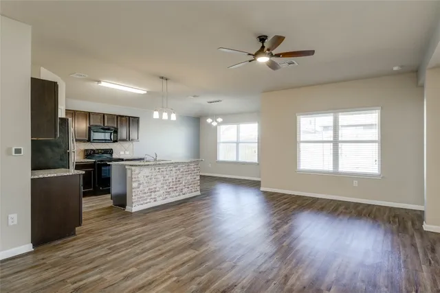 a kitchen with stainless steel appliances kitchen island granite countertop a stove a refrigerator a sink a microwave oven with wooden floor and cabinets