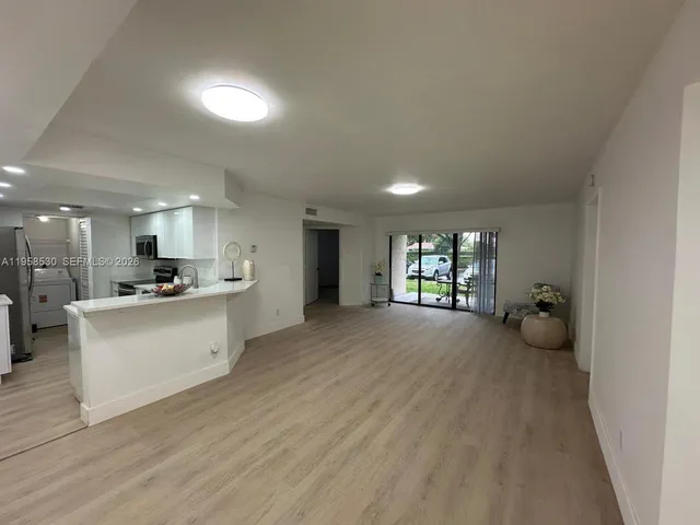 a large living room with stainless steel appliances lots of white furniture a window and a refrigerator