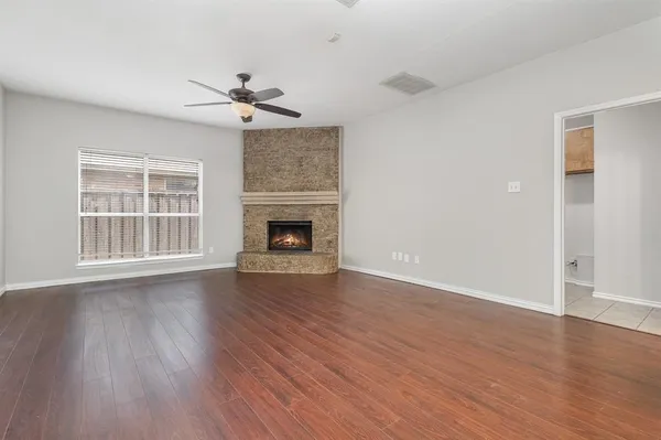 an empty room with wooden floor a ceiling fan a fireplace and windows