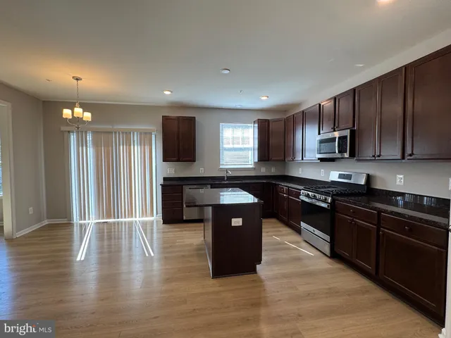 a kitchen with stainless steel appliances granite countertop wooden cabinets a stove a sink and a wooden floor