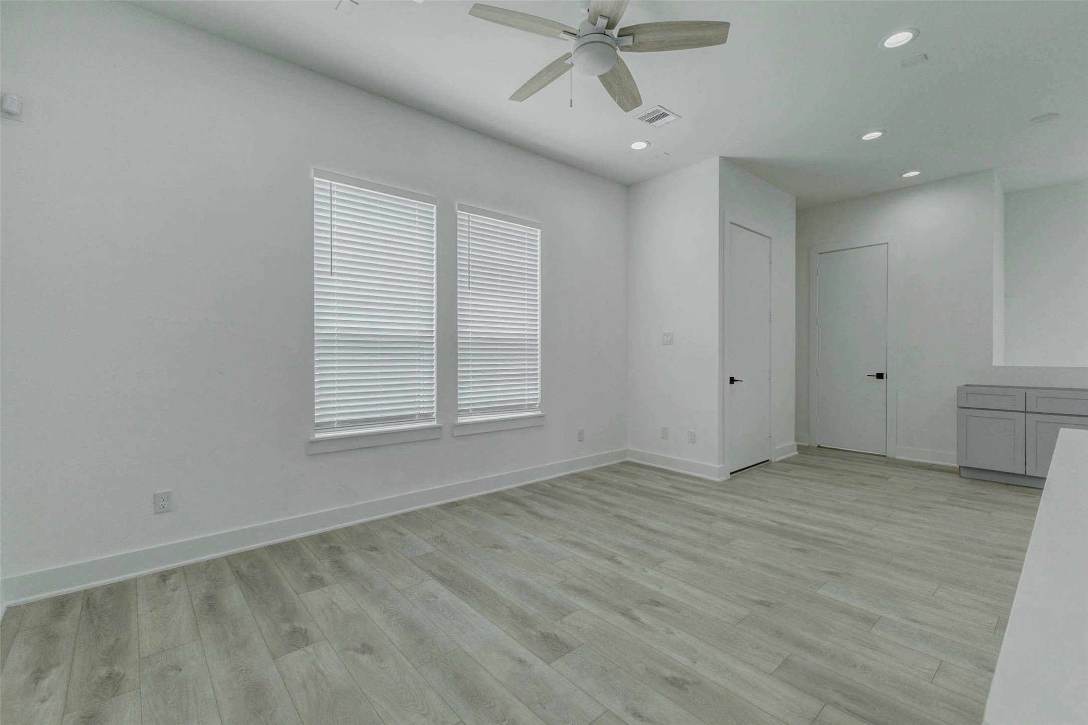 5705 Elysium Street Houston, TX 77091 - Photo 22 of 22 Bright living area with high ceilings, recessed lighting, ceiling fan, large windows with blinds, and seamless light wood-look flooring. The clean white walls and generous open floor plan create an airy, flexible space that can easily accommodate a living room, dining setup, or personalized entertaining area.