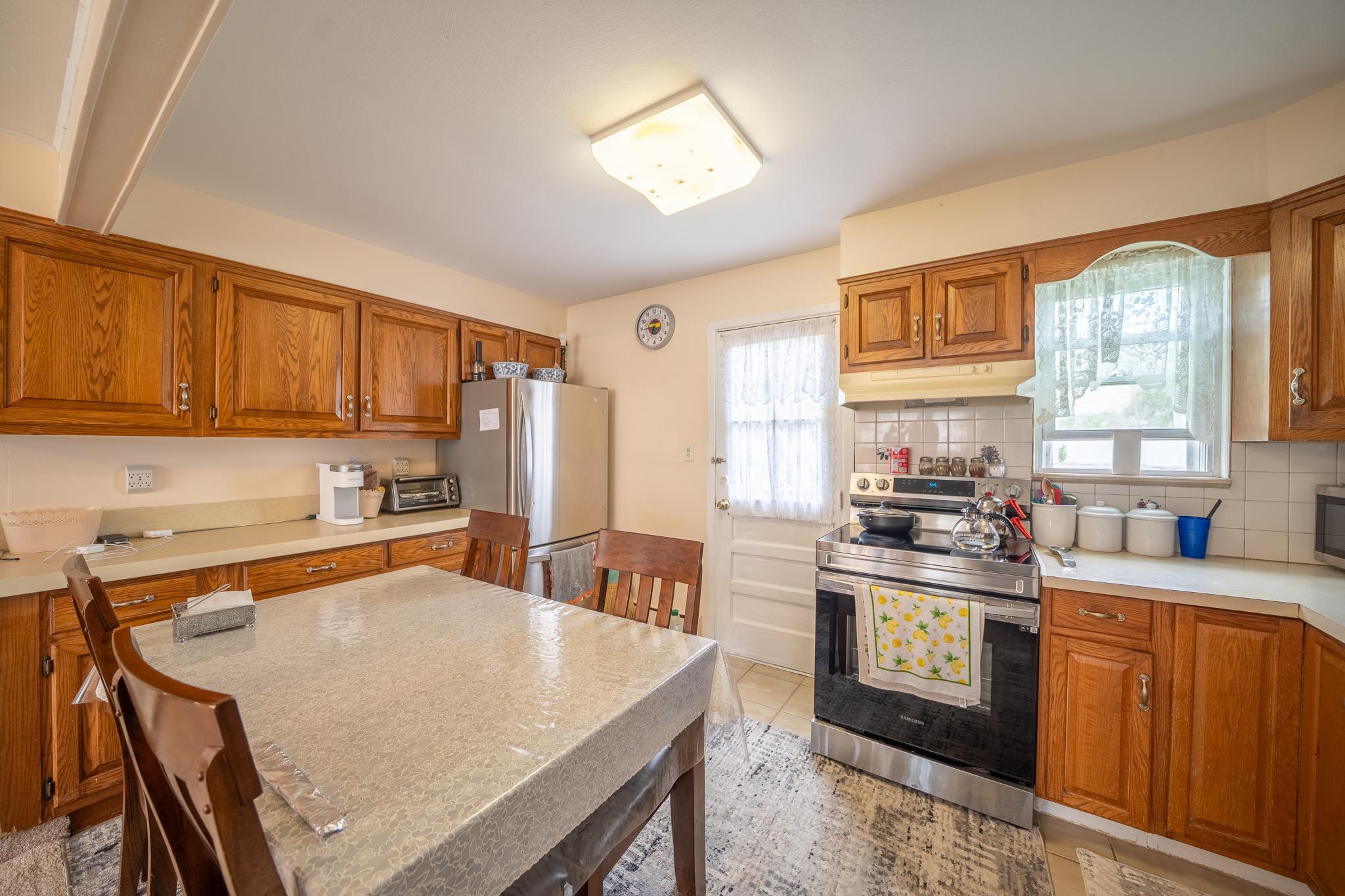47 Cardinal Road Levittown, NY 11756 - Photo 5 of 27 Kitchen featuring appliances with stainless steel finishes, under cabinet range hood, brown cabinetry, light countertops, and backsplash