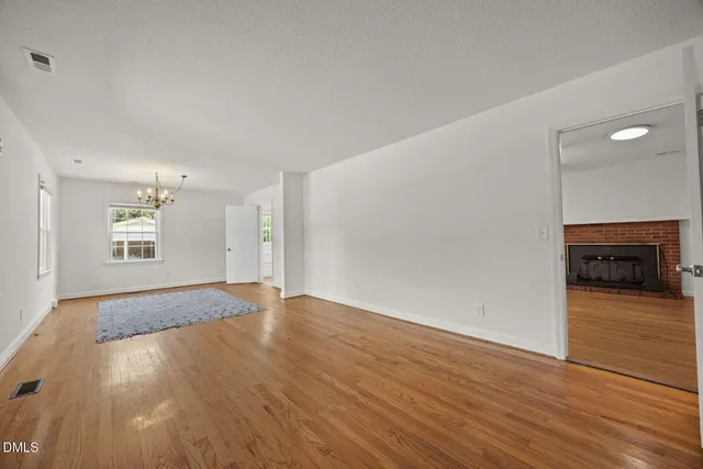 a view of an empty room with wooden floor fireplace and a window