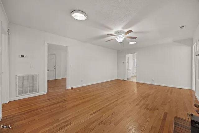 a view of an empty room with chandelier fan and wooden floor