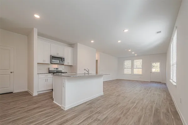 a large kitchen with stainless steel appliances granite countertop a stove top oven a sink dishwasher and white cabinets with wooden floor