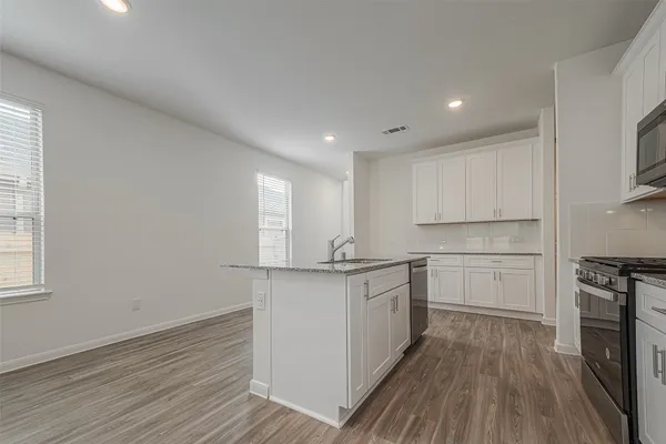 a kitchen with stainless steel appliances granite countertop a stove a sink and white cabinets with wooden floor