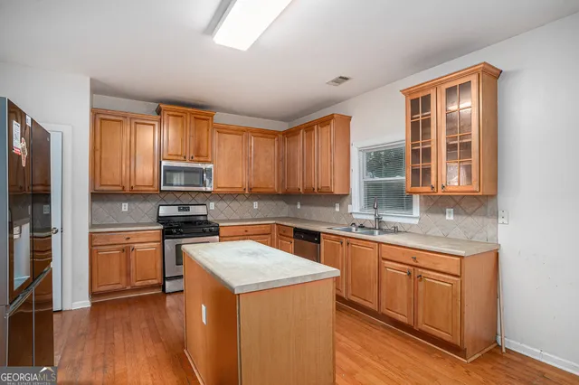 a kitchen with granite countertop wooden floors stainless steel appliances a sink and a window