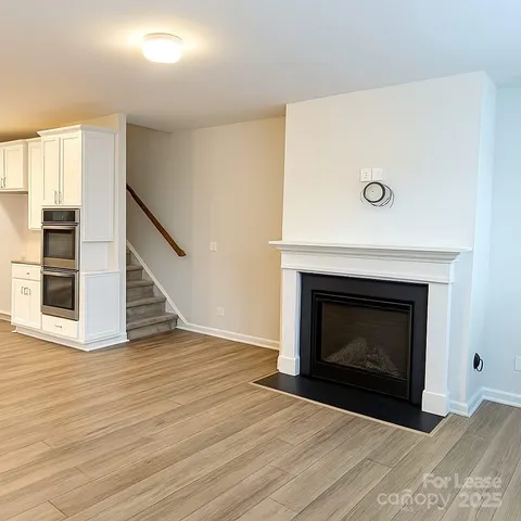 a view of an empty room with wooden floor fireplace and a window