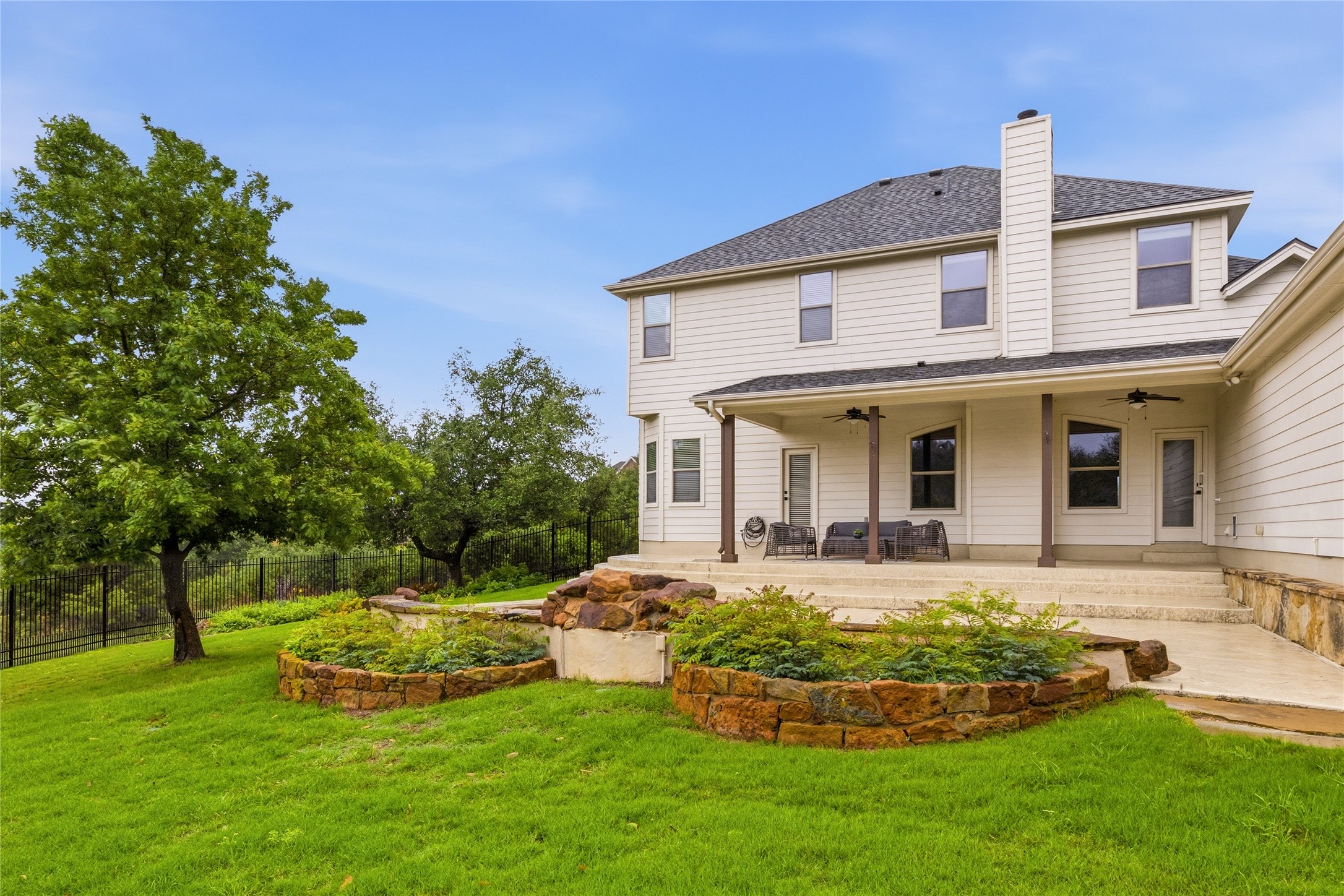 1432 Tom Sawyer Road Austin, TX 78737 - Photo 29 of 33 A spacious elevated patio overlooks a verdant terraced yard with mature trees and stone planters.