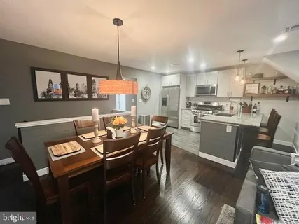 a room with stainless steel appliances kitchen island granite countertop a sink a stove a dining table and chairs with wooden floor