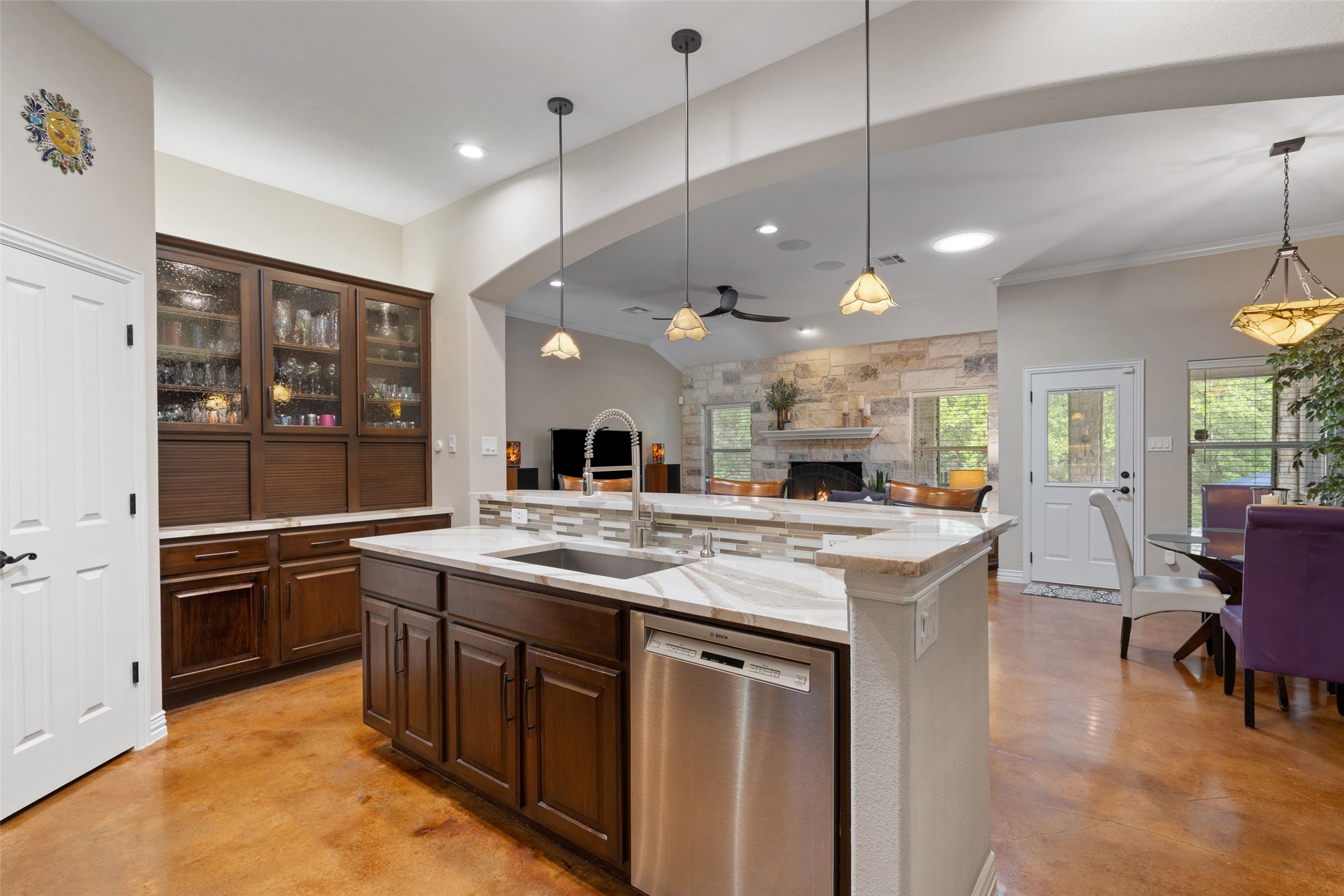 15208 Nightingale Lane Austin, TX 78734 - Photo 11 of 40 Kitchen with finished concrete flooring, dark wood finish cabinets, a ceiling fan, stainless steel dishwasher, and a fireplace