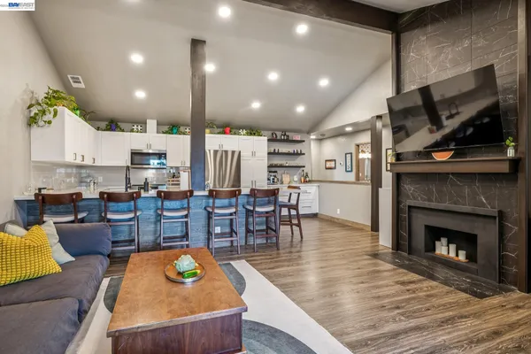 a living room with stainless steel appliances furniture a fireplace a flat screen tv and a kitchen view