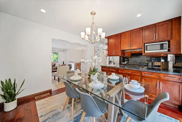 a kitchen with stainless steel appliances granite countertop a refrigerator a sink dishwasher a dining table and chairs with wooden floor